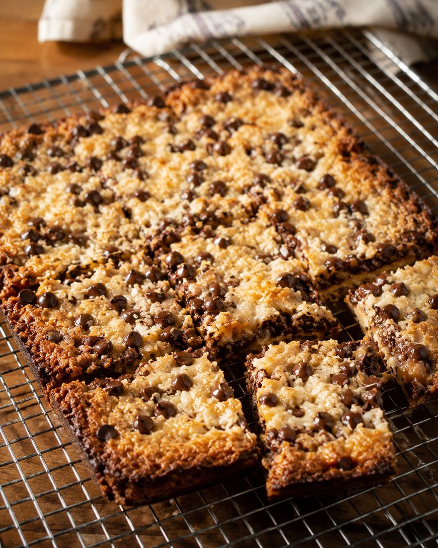 A batch of golden-brown coconut chocolate chip bars cooling on a wire rack, with several squares cut and slightly separated from the rest.