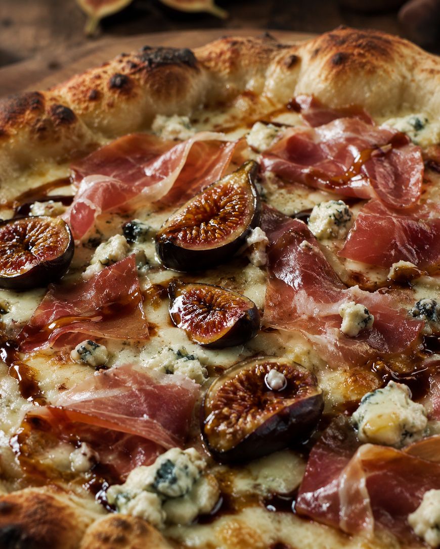 A close-up of a gourmet pizza topped with prosciutto, fresh figs, blue cheese, and a drizzle of balsamic glaze on a golden, puffy crust.