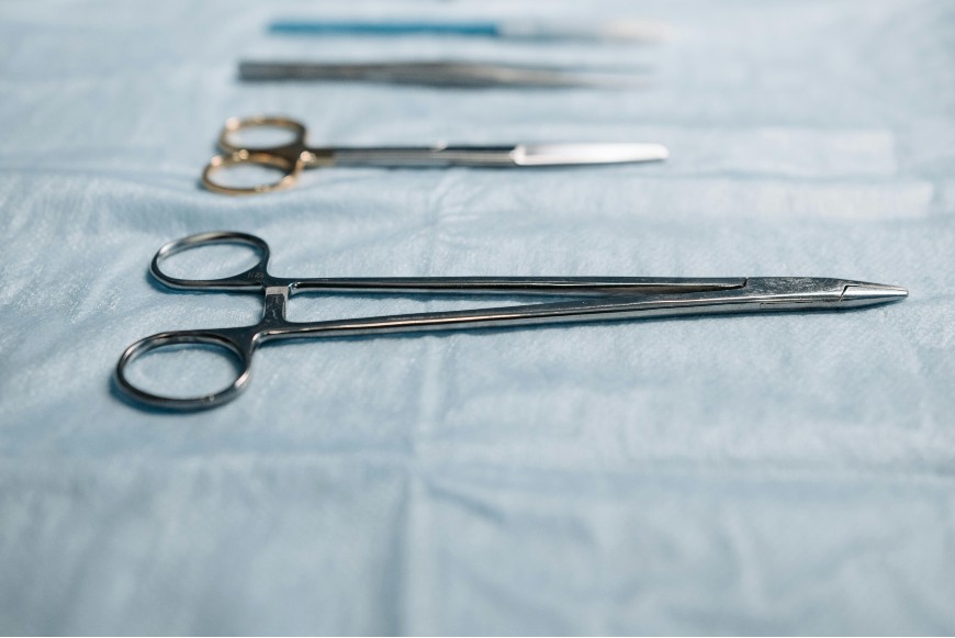 Surgical instruments, including forceps and scissors, are laid out in a row on a blue sterile drape, ready for use in a medical procedure.