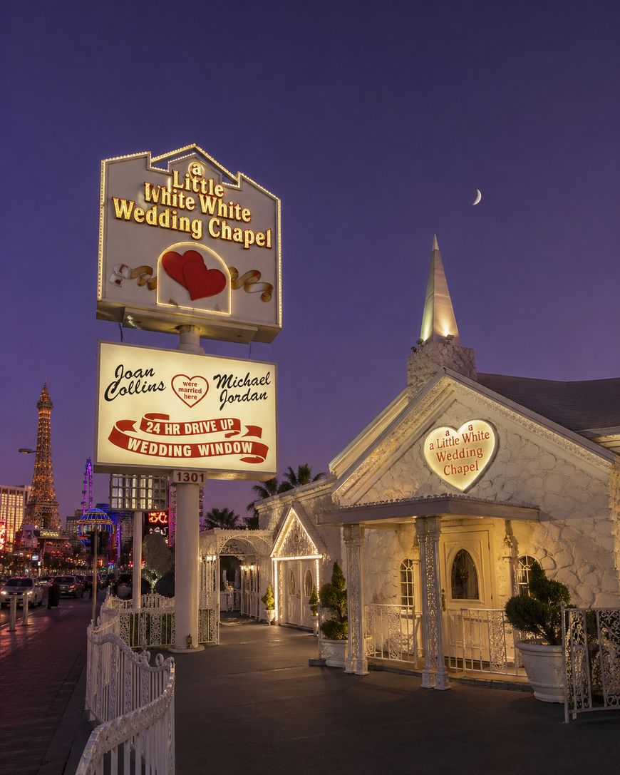 A white chapel with illuminated signs reading “The Little White Wedding Chapel” and listing famous names is shown at dusk in Las Vegas, with the Eiffel Tower replica visible in the background and a crescent moon in the sky.