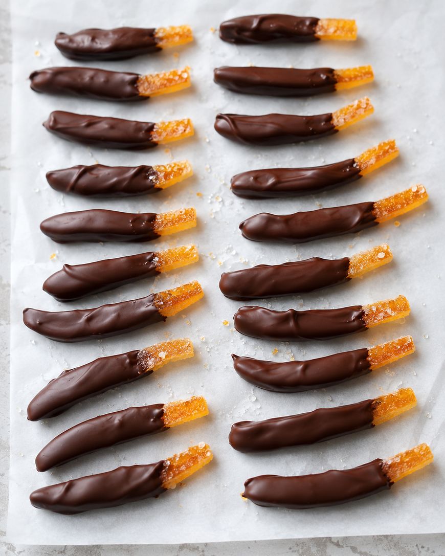 Candied orange peels partially dipped in dark chocolate, arranged in neat rows on a sheet of parchment paper. The sugared ends are exposed, contrasting with the glossy chocolate coating.