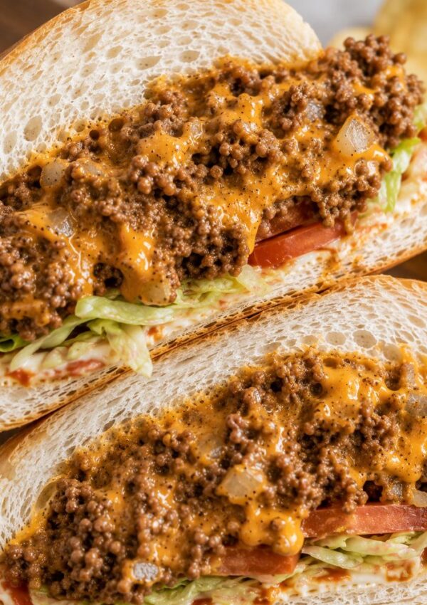 Two sandwiches filled with chopped lettuce, tomato slices, and a savory chopped cheese sandwich recipe of seasoned ground beef topped with melted cheese. The filling is piled thickly on soft white sandwich rolls.