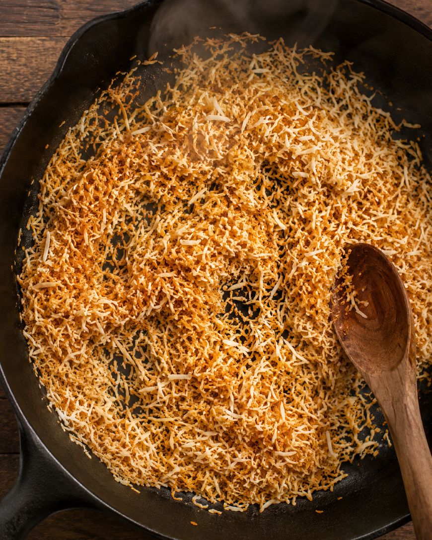 Toasted shredded coconut in a black cast iron skillet with a wooden spoon, sitting on a wooden surface.