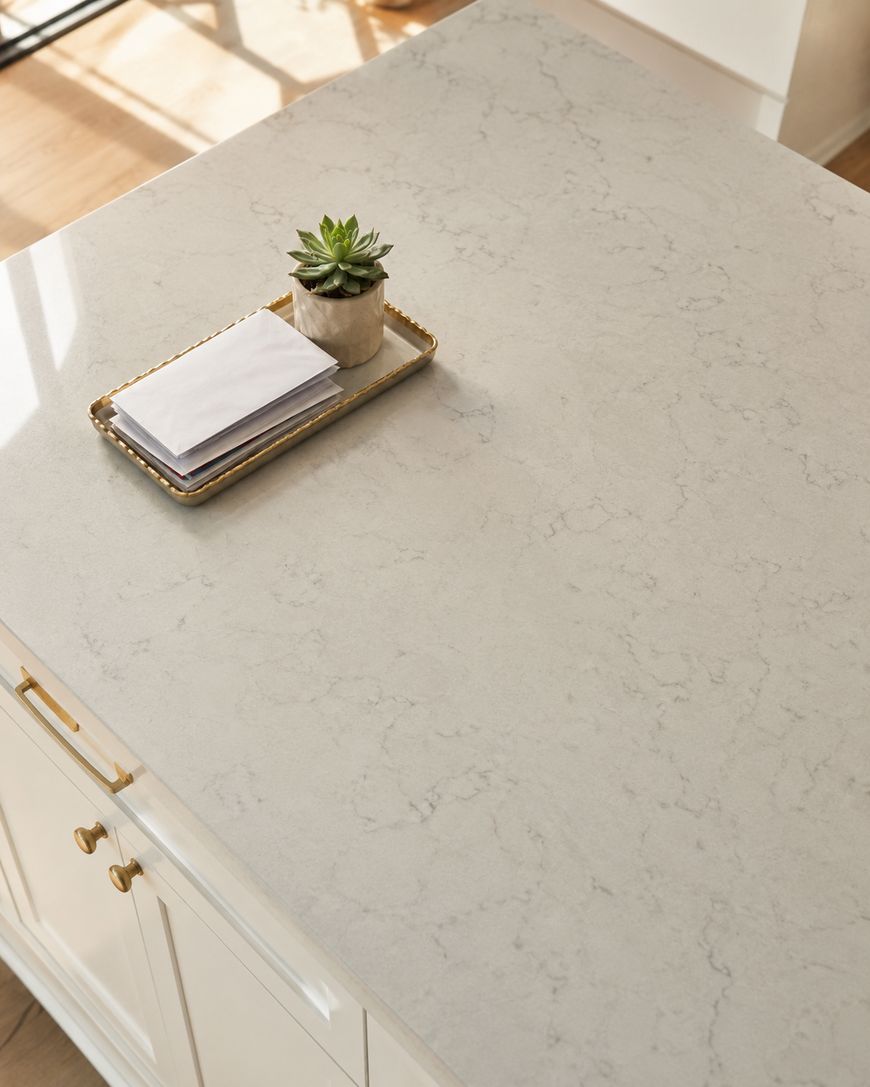 A marble-look kitchen countertop with a small tray holding a potted succulent, a stack of napkins, and a few papers, set in a bright, sunlit room.
