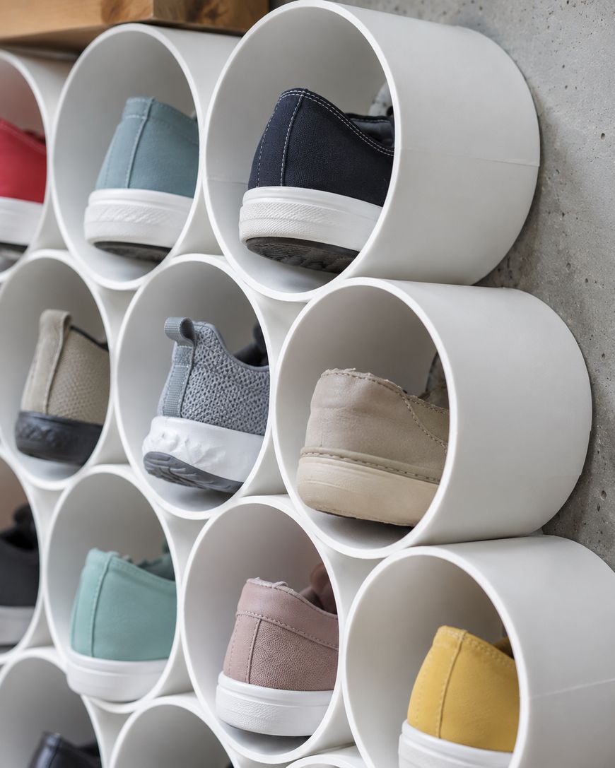 Close-up of a shoe organizer made of round white tubes, each holding a pair of shoes of various colors and styles, neatly arranged against a wall.