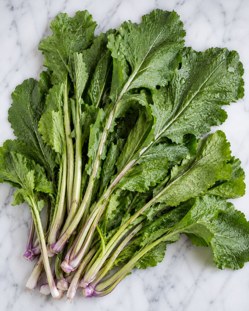 A bundle of fresh mustard greens with long, pale green stems and large, textured green leaves, laid out on a white marble surface.