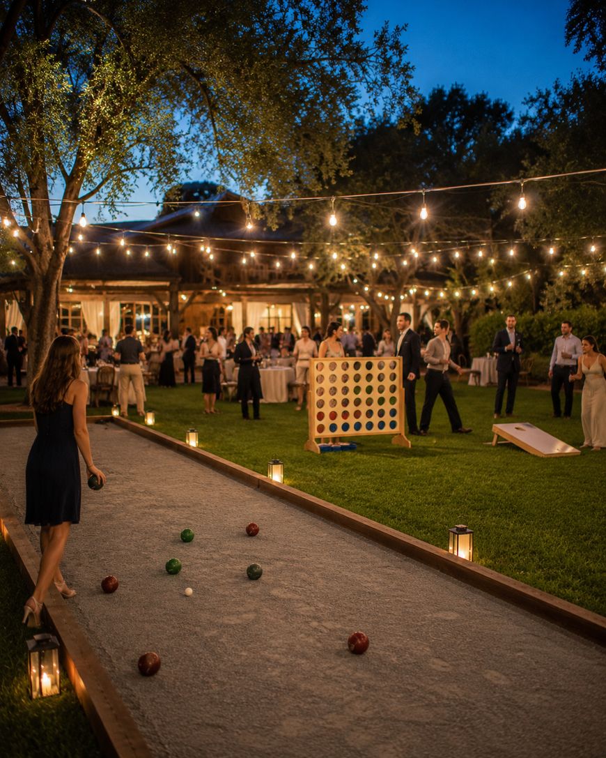 Guests enjoy an outdoor evening event with string lights, playing lawn games like bocce ball, giant Connect Four, and cornhole. People gather near tables and a pavilion in a festive garden setting.