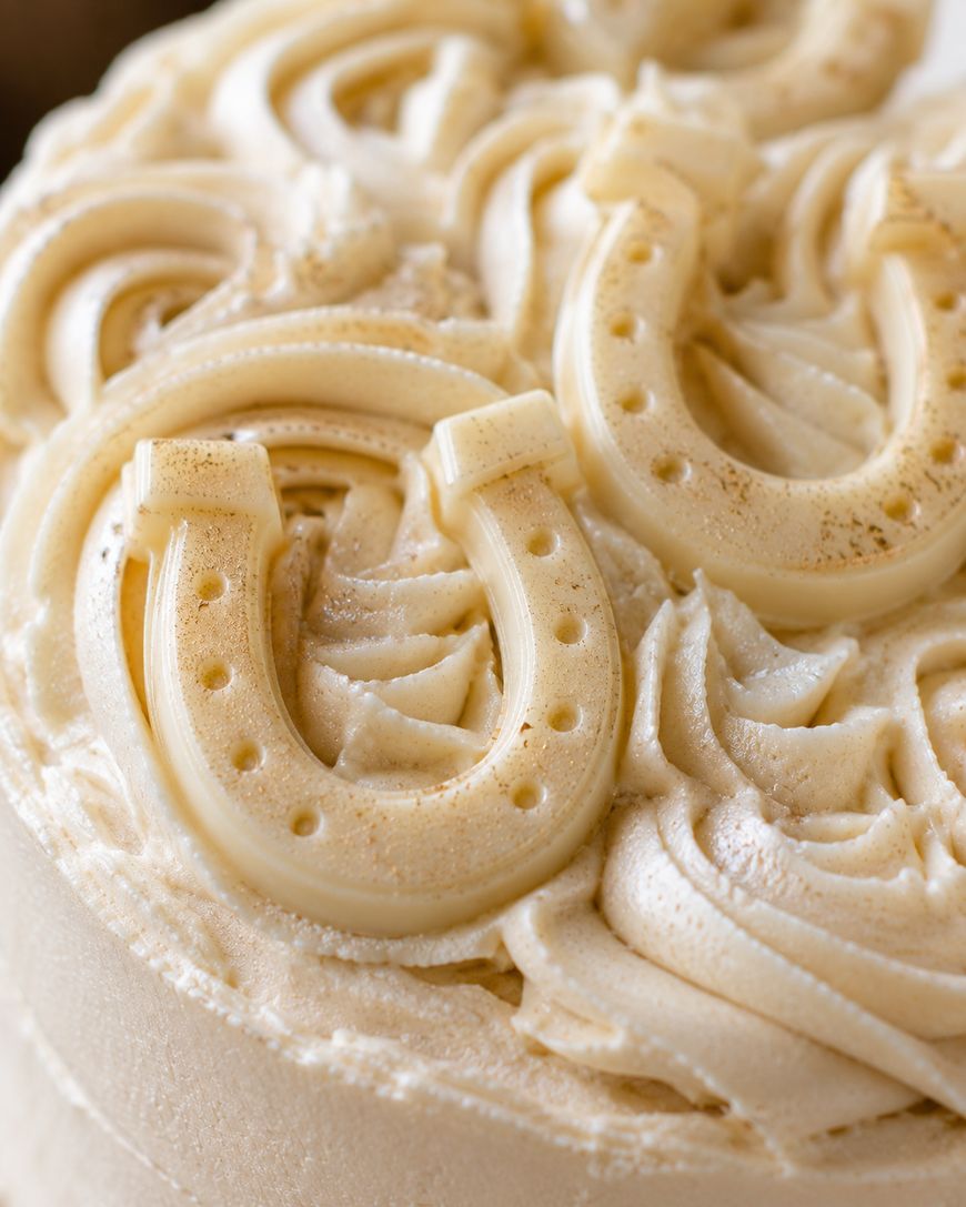 Close-up of a cake topped with creamy swirls and white chocolate horseshoe decorations.
