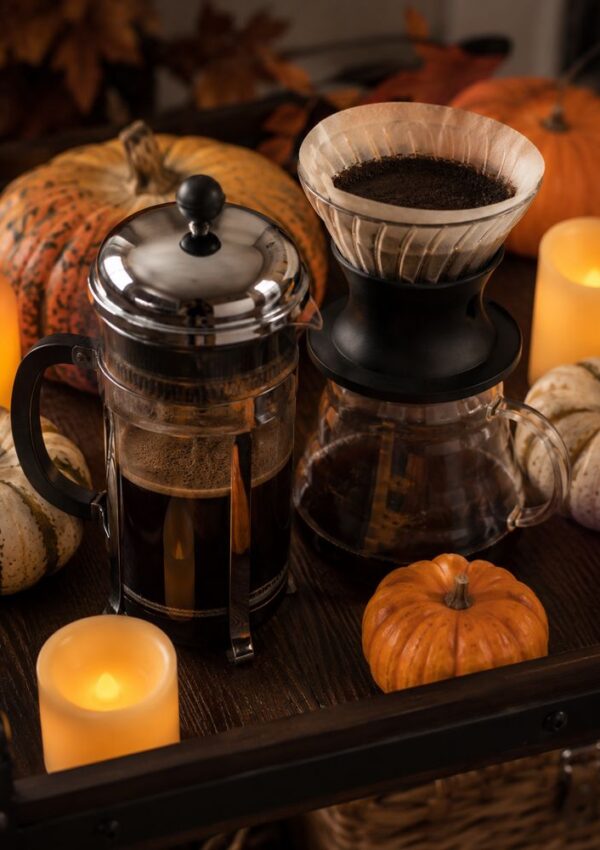 French press and pour-over coffee makers on a wooden table, surrounded by pumpkins, candles, and autumn decor, creating a cozy fall atmosphere.
