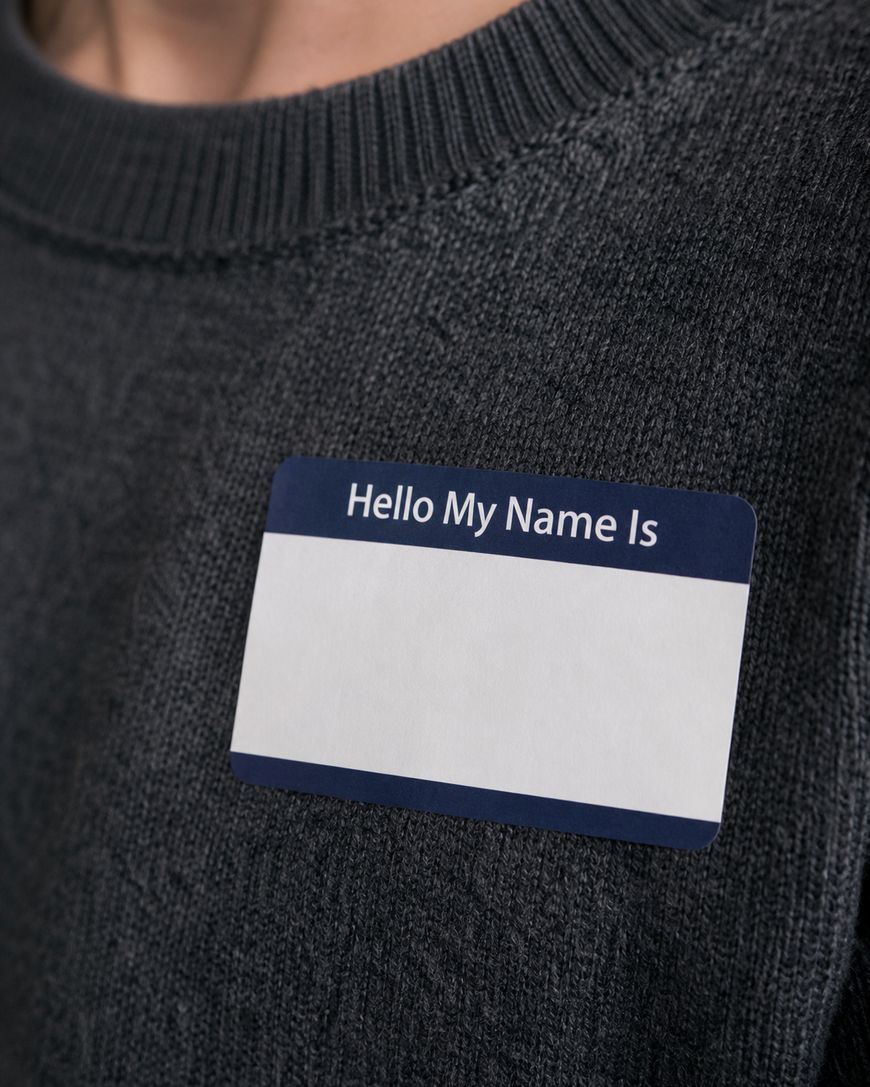 A close-up of a person wearing a dark sweater with a blank Hello, My Name Is name tag sticker on their chest.