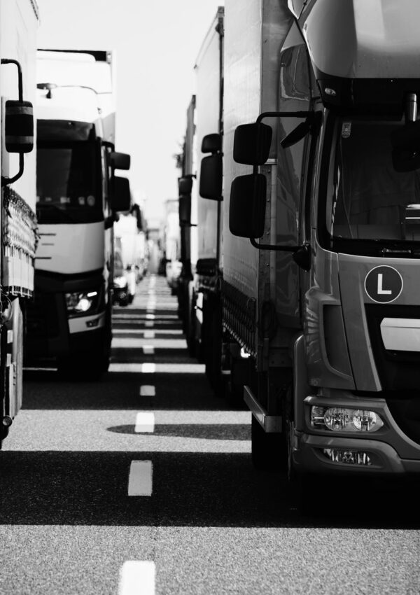 Black and white photo of several large trucks parked closely together on a road, creating a corridor in the center. The image captures the front and sides of the vehicles from a low angle, highlighting the reliable infrastructure that supports local business and transportation.