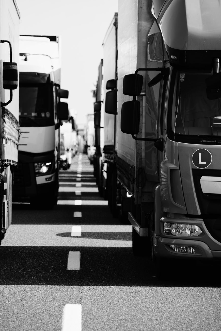 Black and white photo of several large trucks parked closely together on a road, creating a corridor in the center. The image captures the front and sides of the vehicles from a low angle, highlighting the reliable infrastructure that supports local business and transportation.