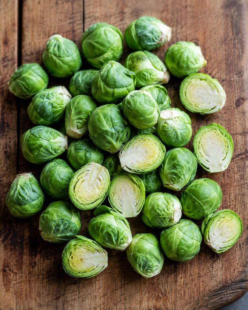 A pile of fresh Brussels sprouts, some whole and some cut in half, arranged on a rustic wooden surface.