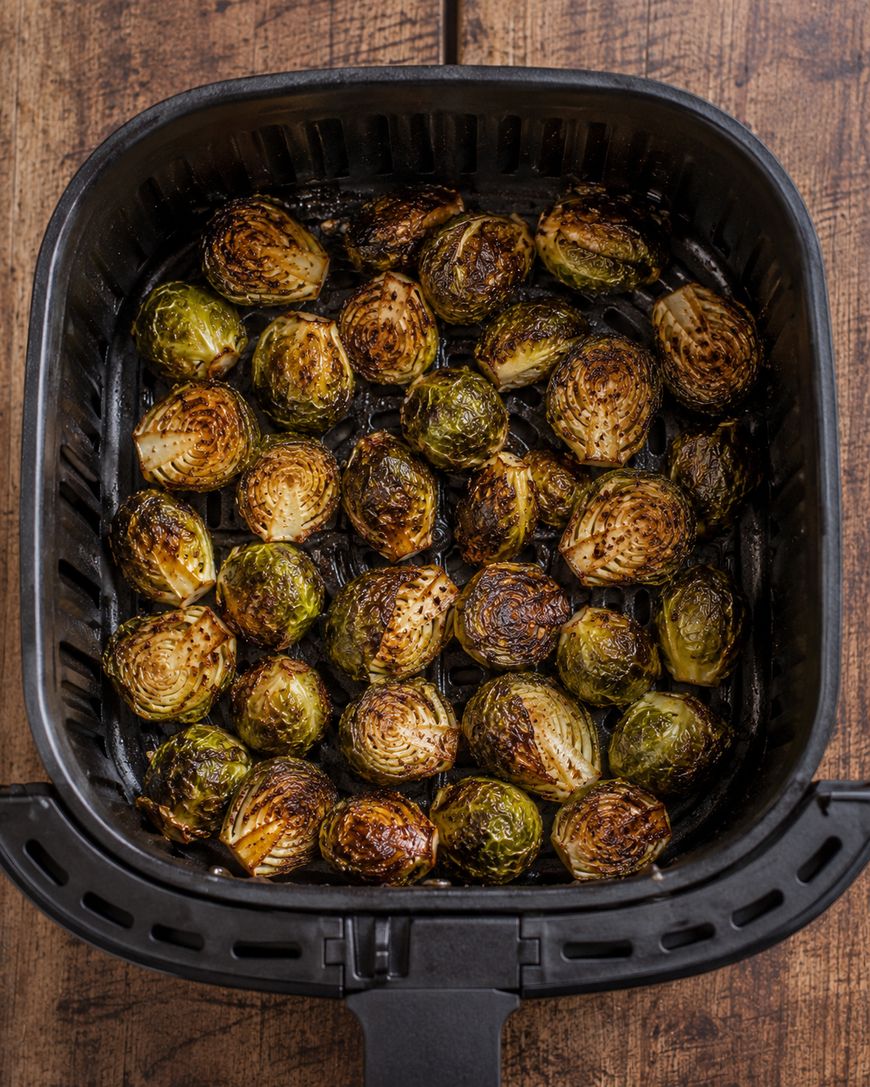 Crispy, roasted Brussels sprouts halves inside a black air fryer basket on a wooden surface.