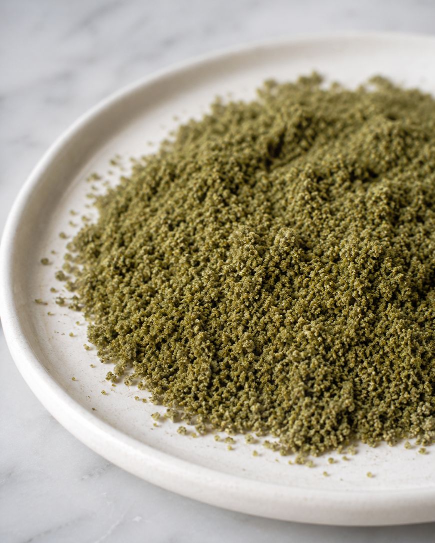 A close-up of a white plate filled with a mound of fine green powder, resting on a marble surface.
