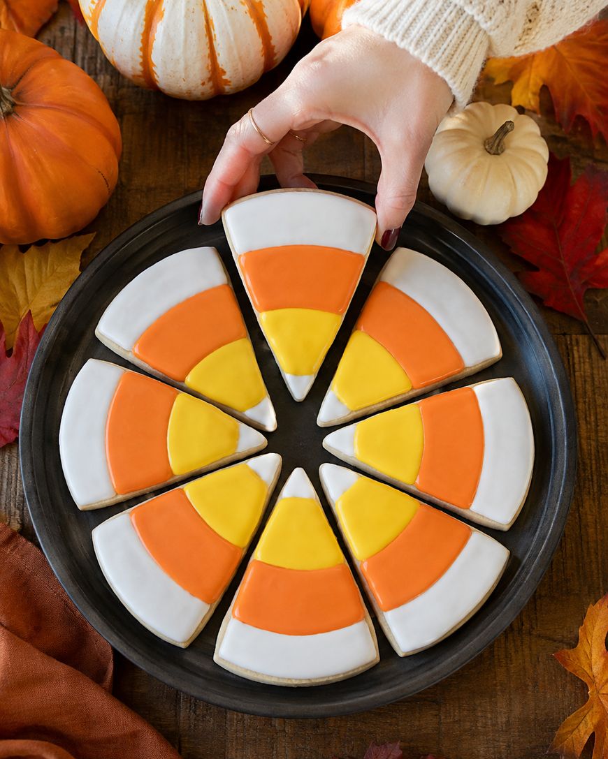 A hand lifts a candy corn-shaped cookie from a plate