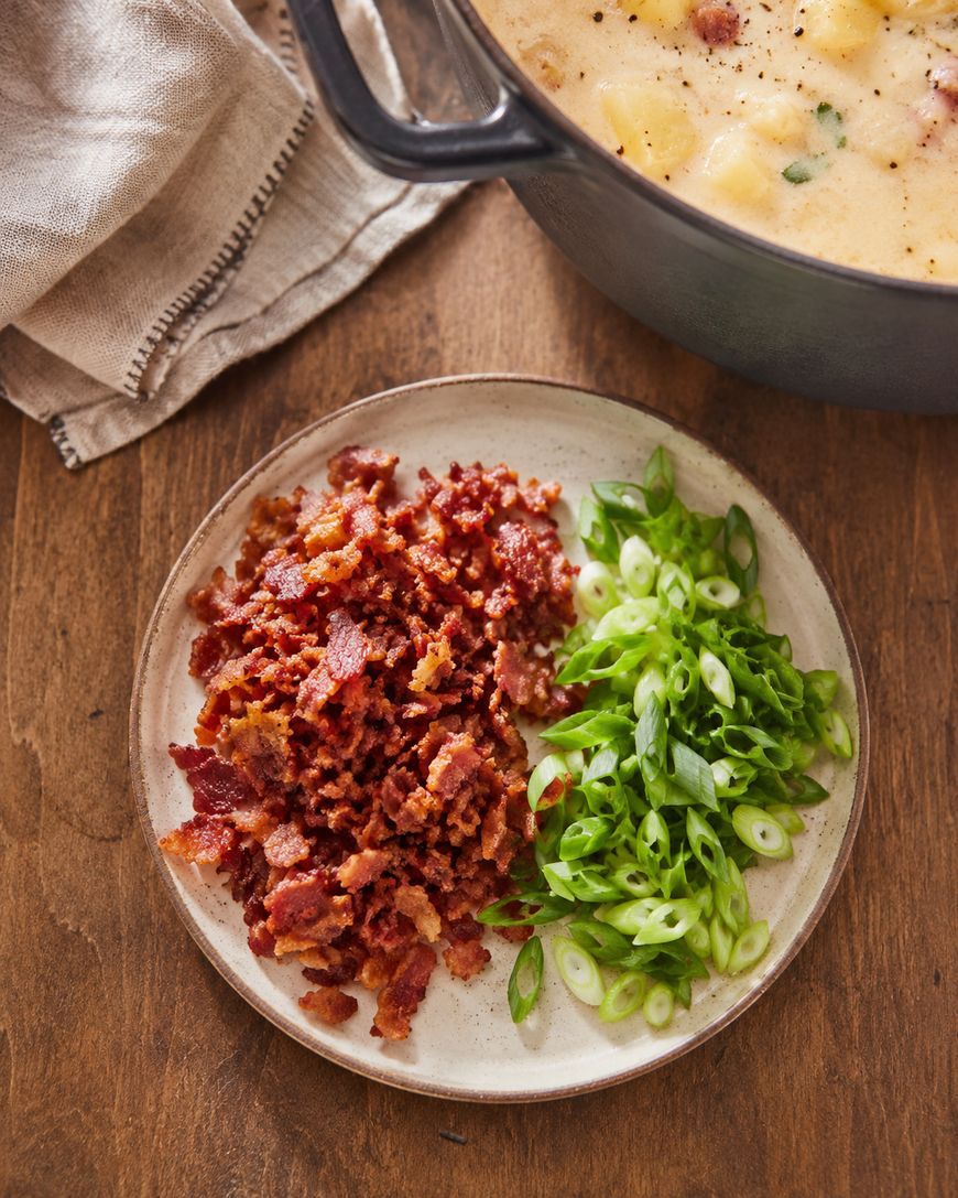 A plate of crispy bacon bits and sliced green onions next to a pot of soup.