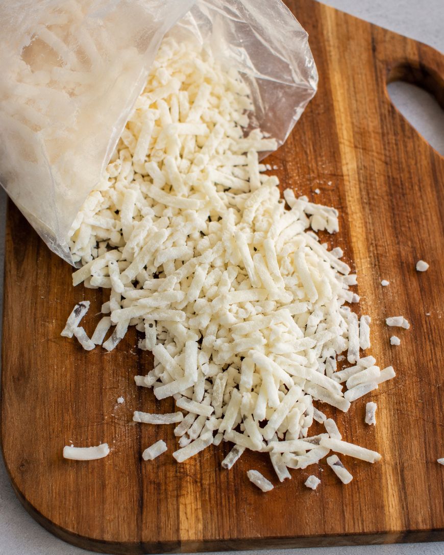 Bag of shredded frozen hash browns spilling onto a wooden cutting board.
