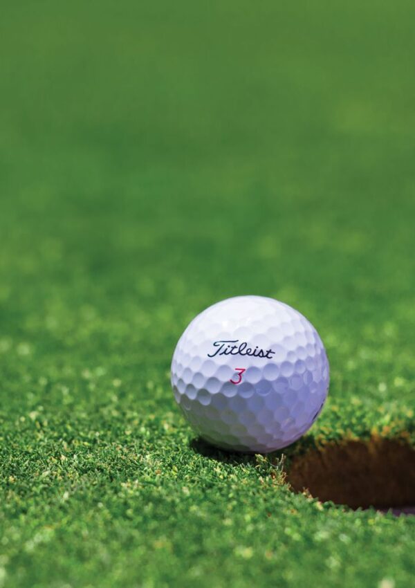 A white Titleist golf ball labeled with a red number 3 rests on green grass near the edge of a golf hole.