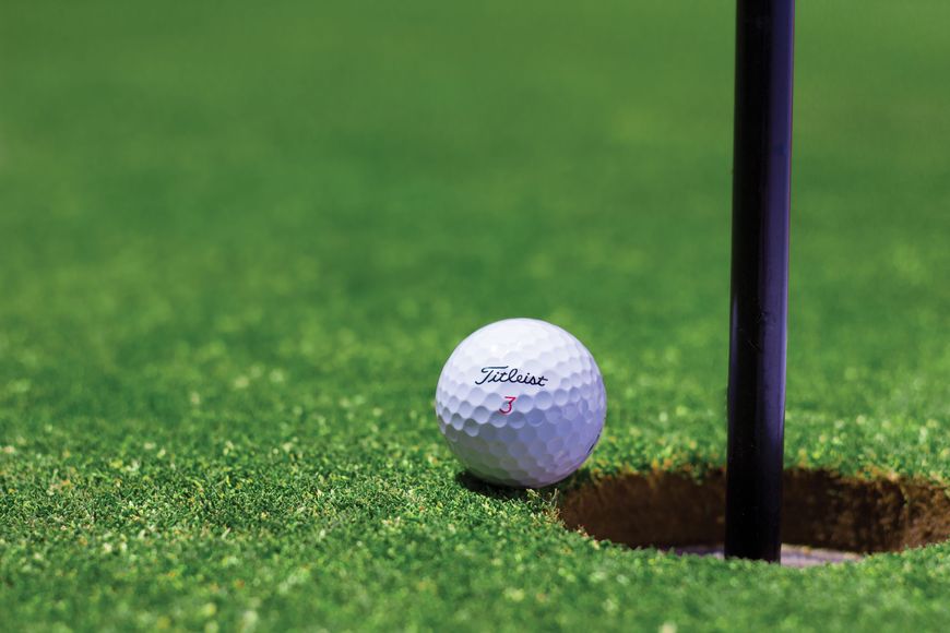 A golf ball sits on the green, right next to the hole and flagstick, about to be putted in.