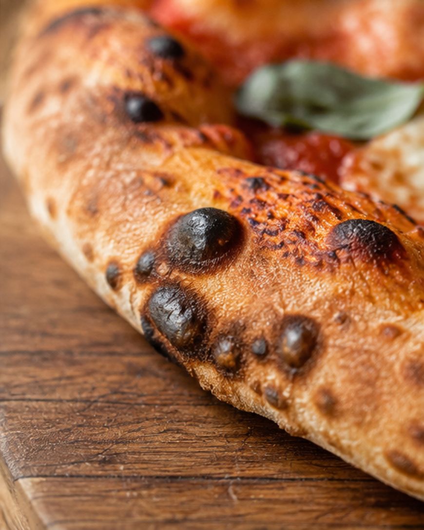 Close-up of a pizza crust with blistered, charred spots, resting on a wooden surface.