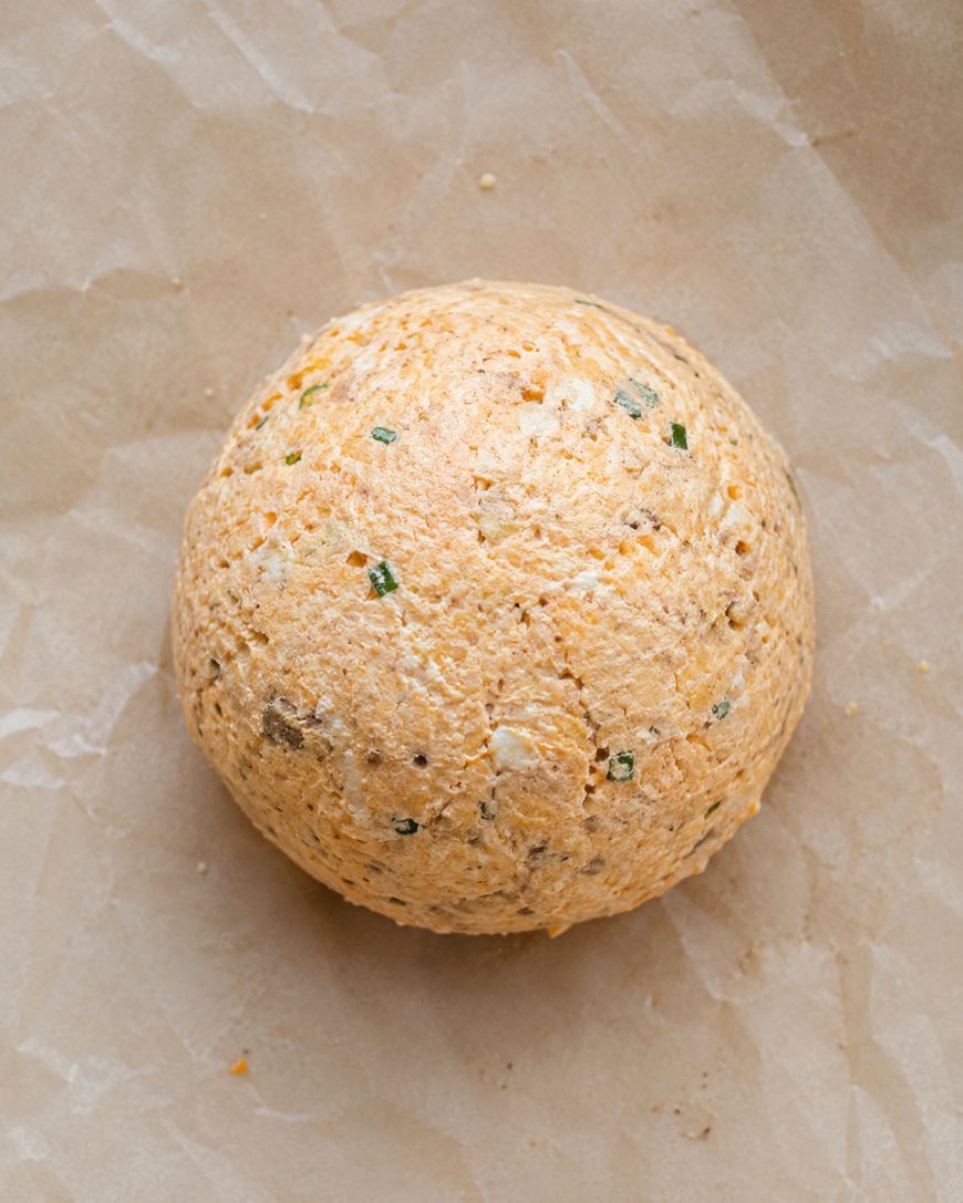 A round ball of cheese mixed with herbs and spices sits on a sheet of crumpled parchment paper.