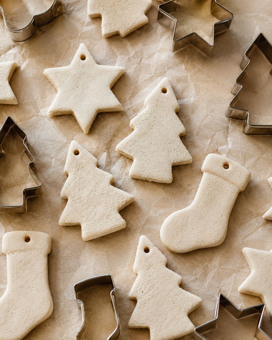 Unbaked holiday cookies shaped like stars, trees, and stockings on parchment paper, surrounded by corresponding metal cookie cutters.