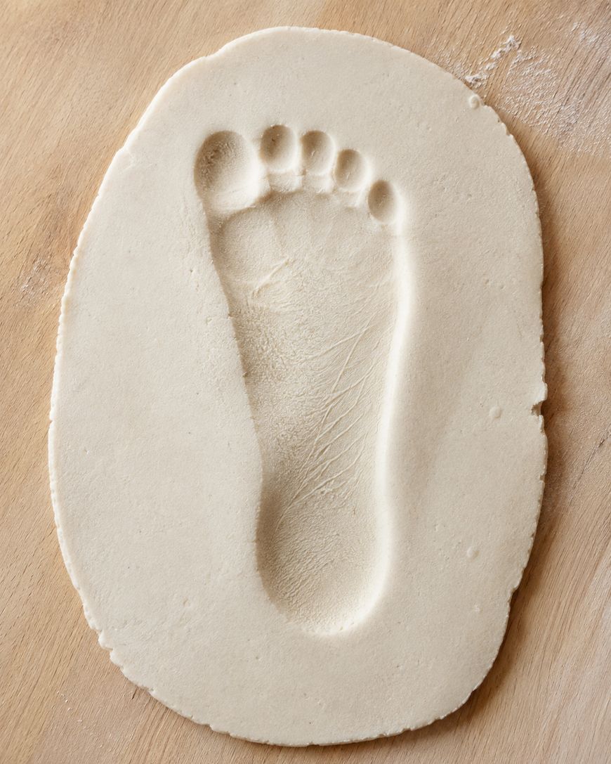 A footprint pressed into a round, flat piece of pale dough or clay, resting on a wooden surface.