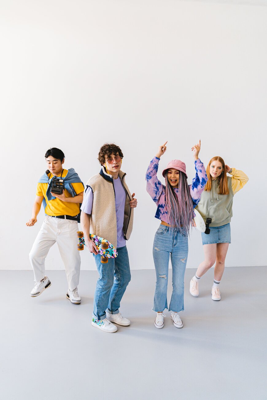 Four friends in colorful retro-style outfits with a vintage camera and skateboard for a decades-theme group costume.
