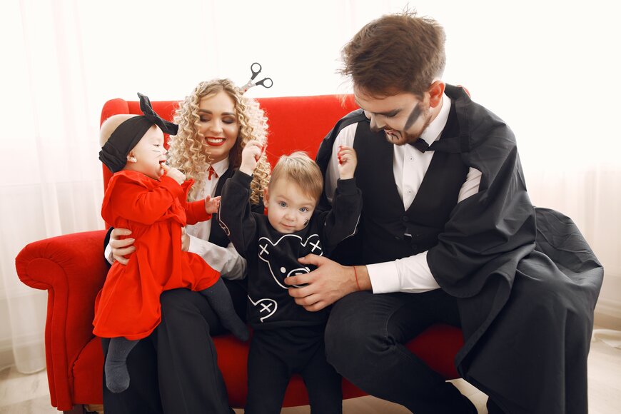 A family of four in Halloween costumes sitting together on a red couch.