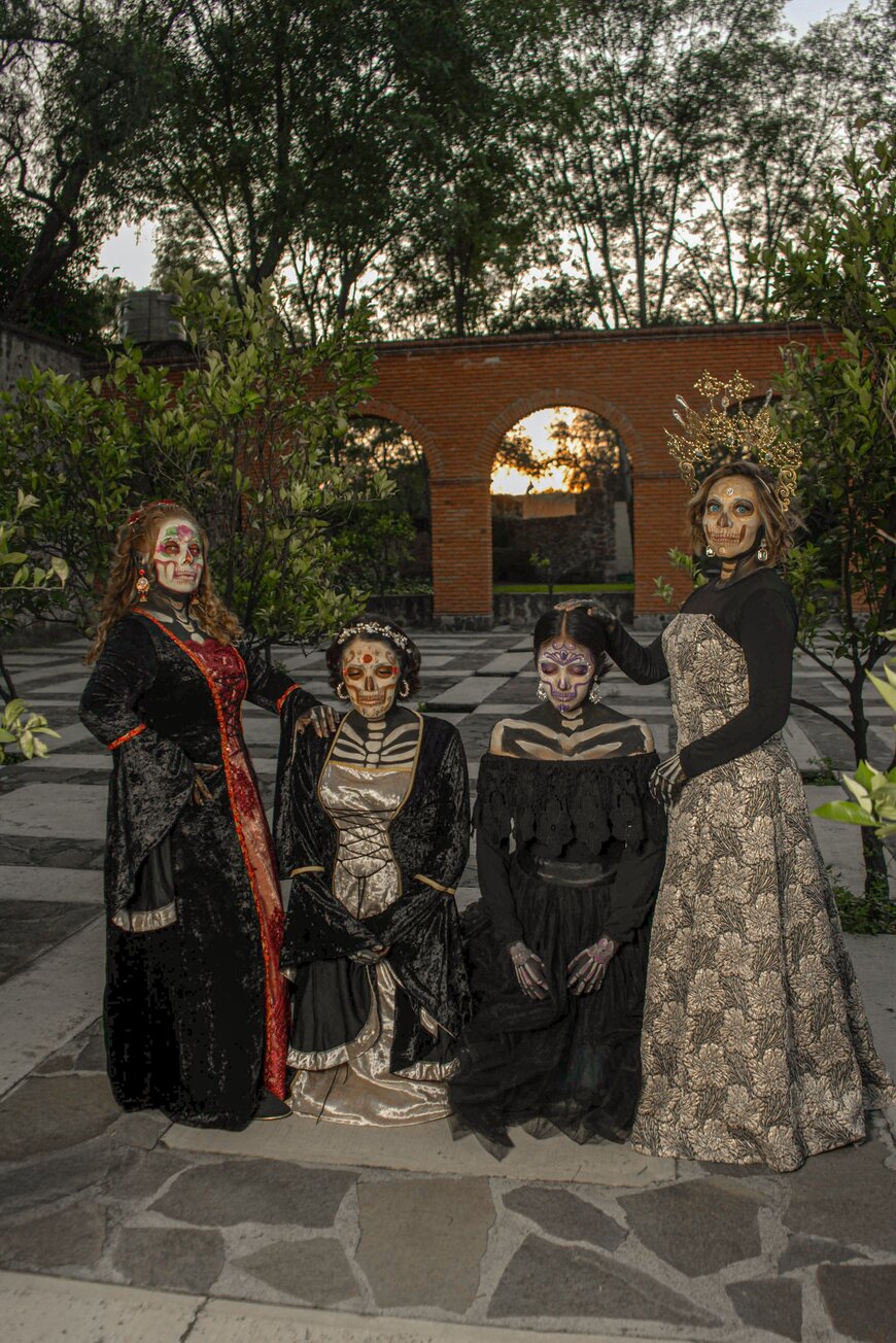 Four people in elegant black outfits with skeleton face paint posing together for Halloween.