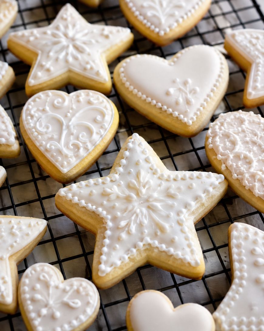 Heart- and star-shaped sugar cookies with intricate white royal icing designs rest on a black wire cooling rack.