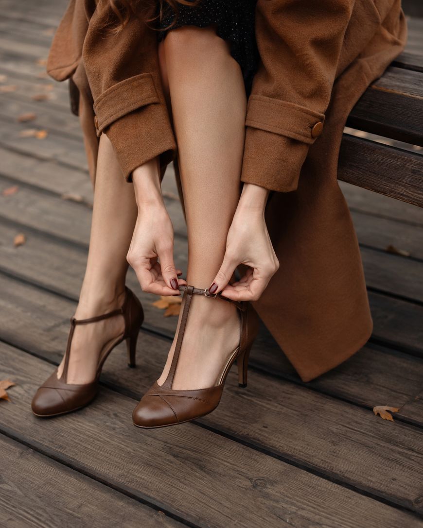 A woman's hands fastening the T-strap on a pair of heeled shoes.