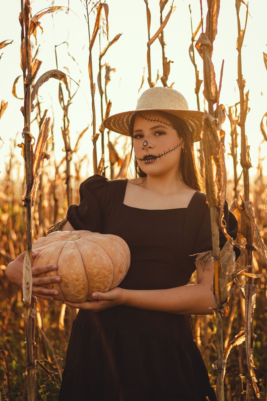 A woman in a straw hat and brown dress standing in a cornfield for an elevated countryside Halloween costume.