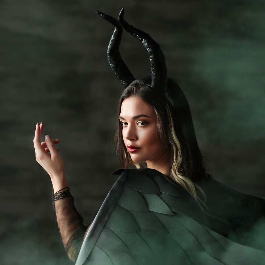 A woman in black horns and a dark green dragon-scale cape for a dramatic dark sorceress Halloween costume.