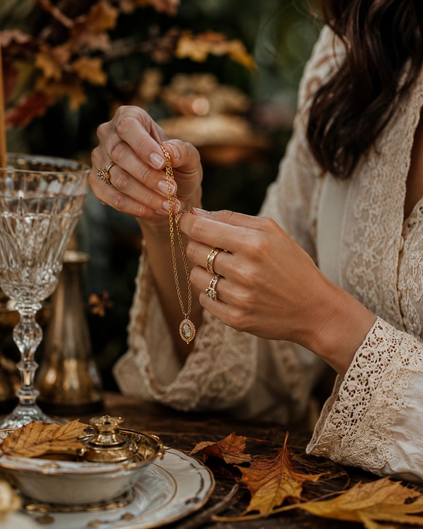 A woman's hands clasping a delicate gold necklace at a styled autumn tablescape.