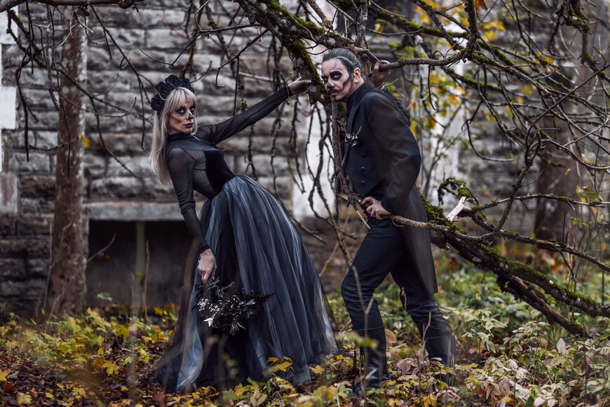 A couple in elaborate black gothic attire with dramatic makeup for a matching Halloween costume.