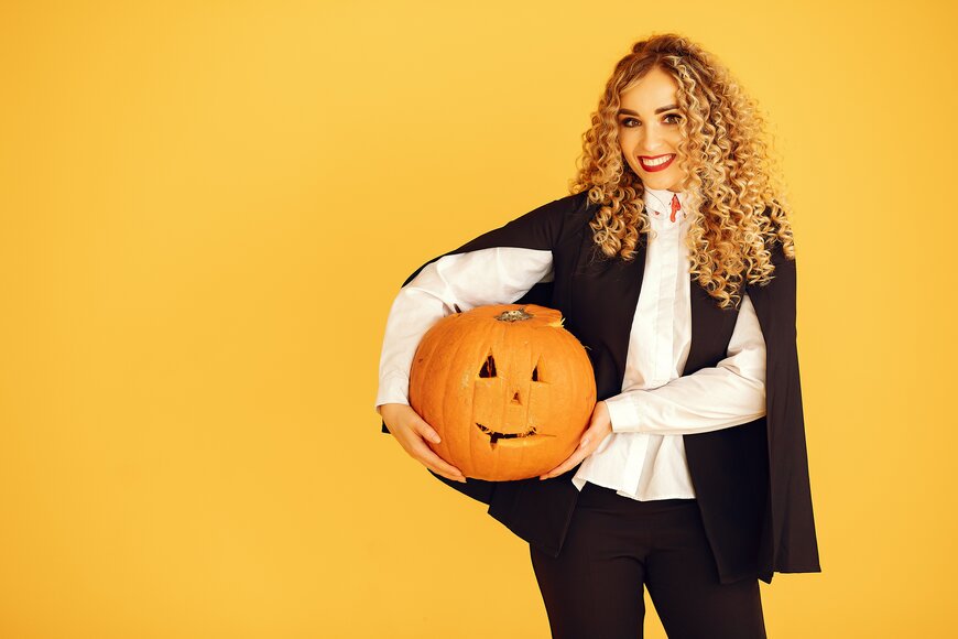 A woman in a black cape and crisp white blouse holding a carved pumpkin for a graphic black-and-white Halloween costume.