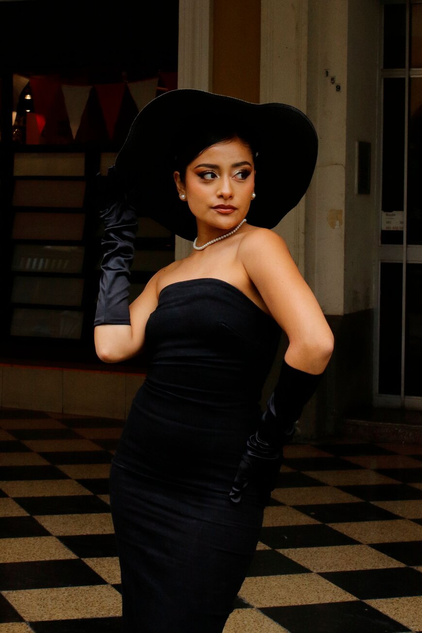 A woman in a strapless black dress, wide-brim hat, pearls, and gloves for an Old Hollywood glamour Halloween costume.