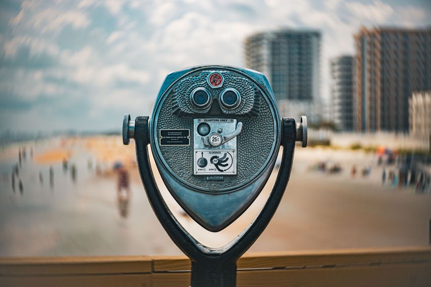 A coin-operated tower viewer overlooks a sandy beach and coastal high-rises on a sunny day.