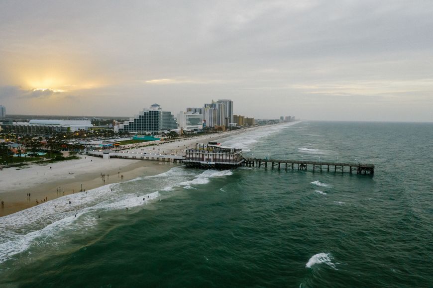 An aerial view of the Daytona Beach pier and boardwalk hotels along the shoreline at dusk.