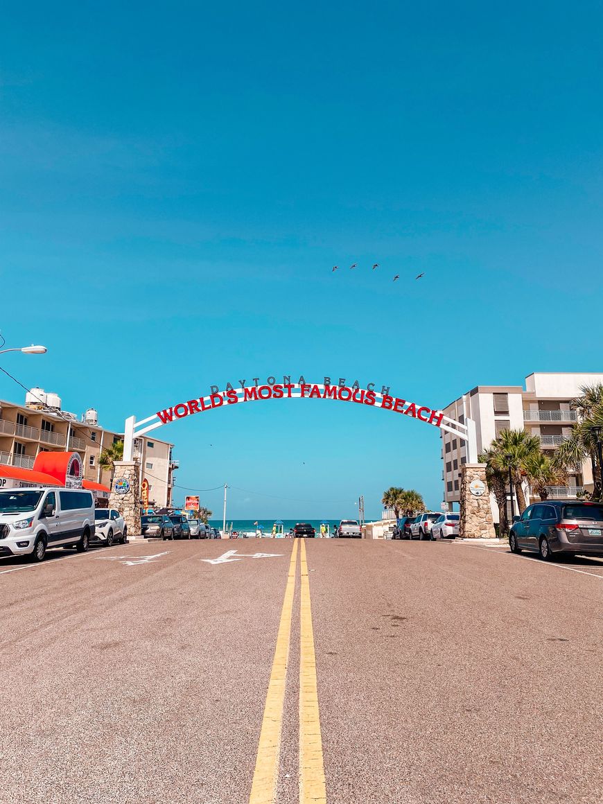 A road leads toward an archway sign reading Daytona Beach, World's Most Famous Beach, with the ocean visible beyond.