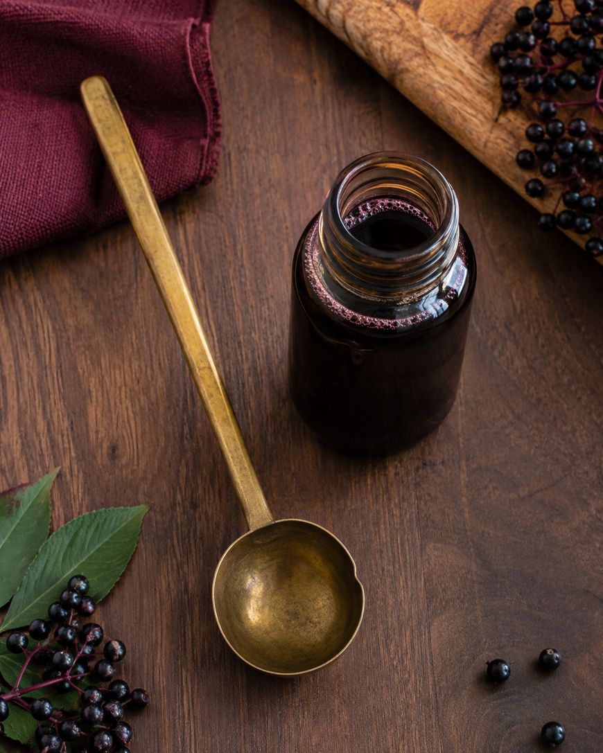 A brass ladle rests beside a glass jar filled with dark liquid on a wooden table.