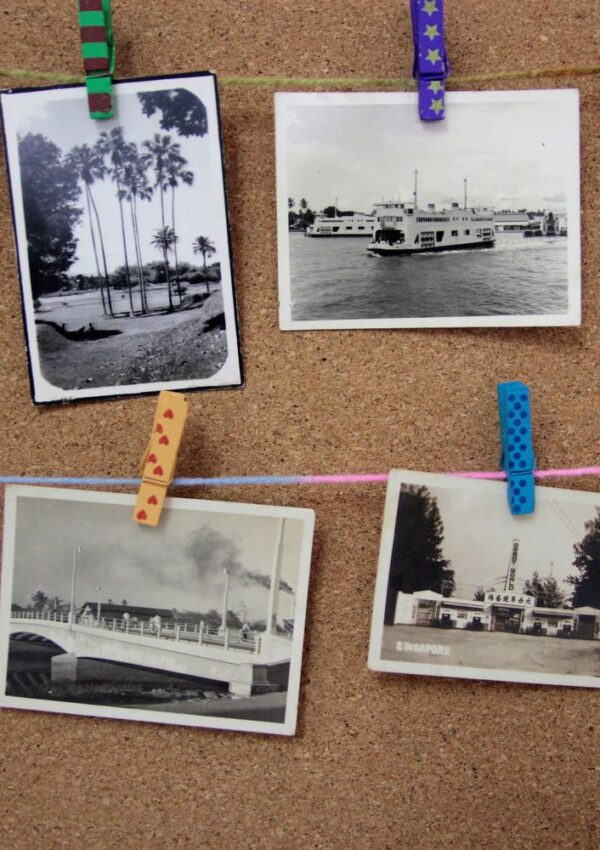 Four black-and-white vintage photos are clipped with colorful clothespins to strings on a corkboard. The images show scenes with boats, bridges, palm trees, and buildings.