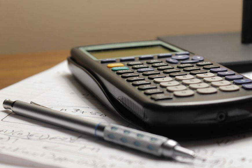 A scientific calculator and a pen rest on papers with handwritten mathematical notes and equations.