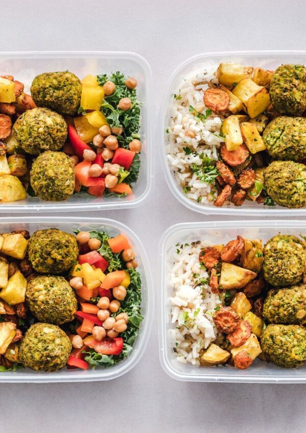 Four meal prep containers filled with rice, falafel balls, roasted potatoes, carrots, chickpeas, chopped red bell pepper, and leafy greens—perfect for back-to-office meal prep or busy schedule meals. The containers are arranged neatly on a light surface.