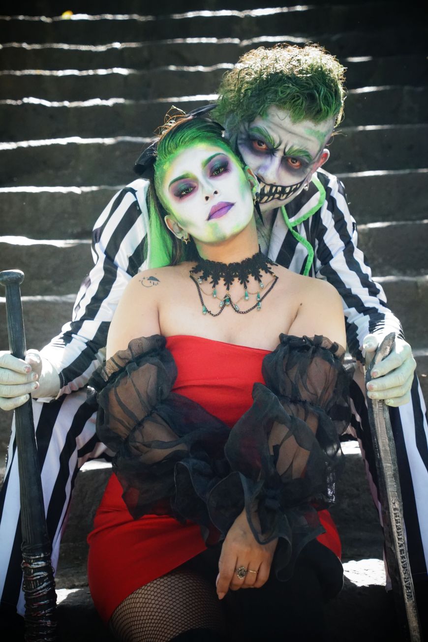 Close up of a couple in green and white Beetlejuice-style face paint and black and white striped costume pieces.