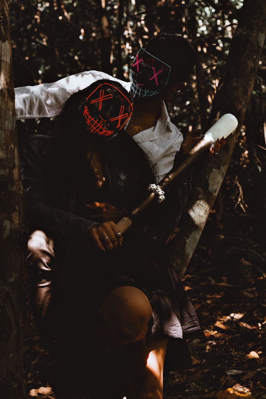 A couple wearing glowing neon wire masks in a dark forest setting.