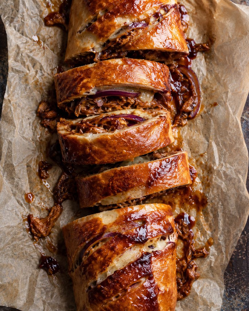 Sliced BBQ pulled pork stromboli with red onion on parchment paper.