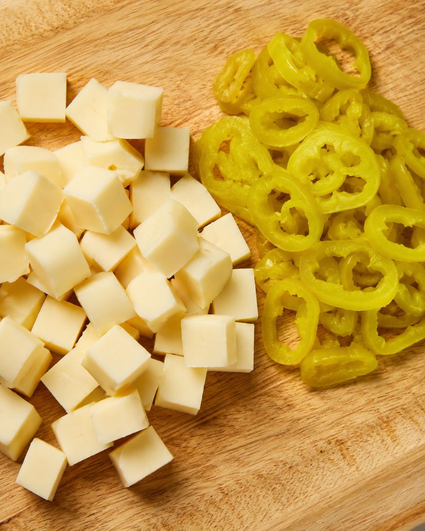 Cubes of cheese and sliced yellow pickled peppers on a wooden cutting board.